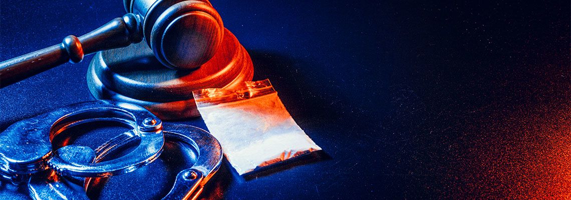 Judge gavel next to handcuffs and small bag of drugs