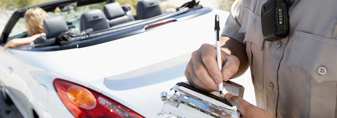 Police officer writing traffic ticket to woman sitting in car