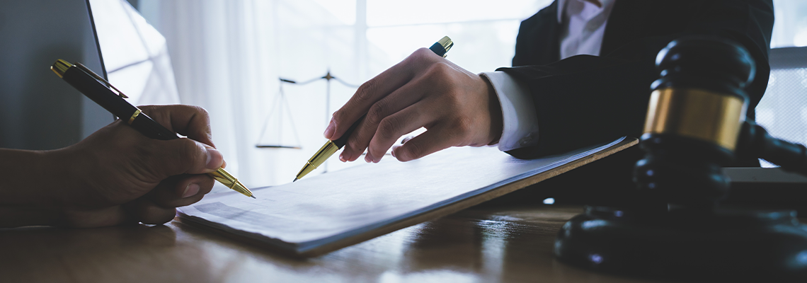 Two hands, one belonging to a legal professional, point to a document for a client to sign