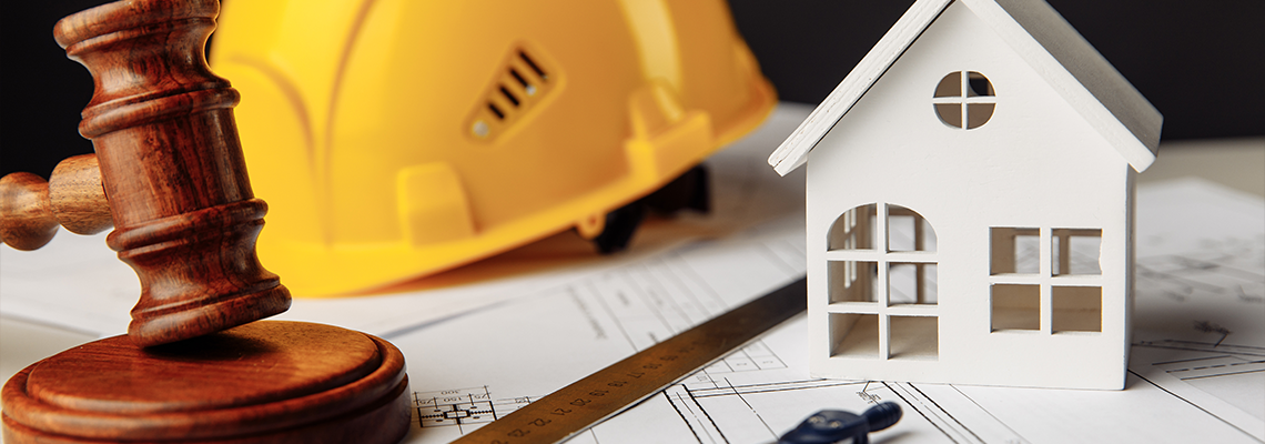 Judge gavel, white house and yellow hard hat with drawing tools on construction plan