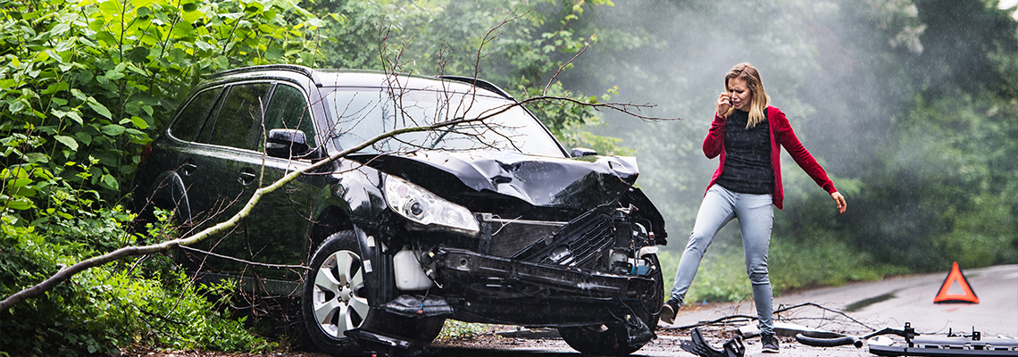 An angry young woman with smartphone by the damaged car