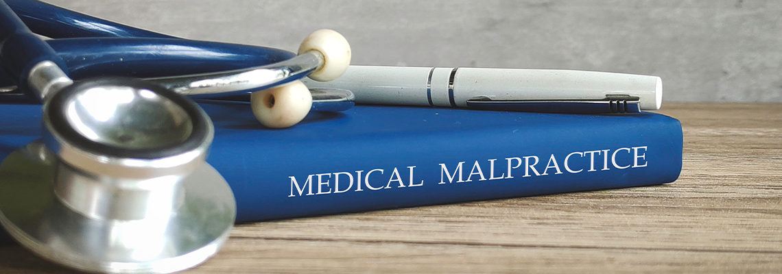 Stethoscope and a pen on a book titled 'MEDICAL MALPRACTICE,'