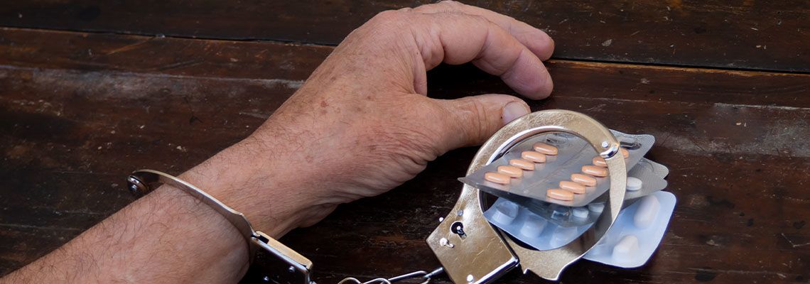 Handcuffed hands of a man with prescription pills