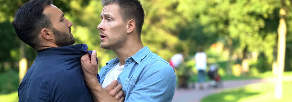 Angry man pushing threatening another male outdoors