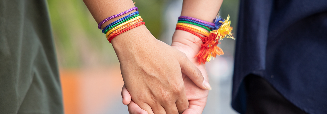 Hand of LGBT Women Holding Together with Rainbow Ribbon Symbol