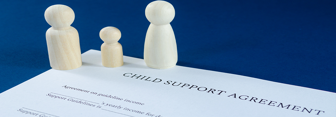 Printed child support agreement with man, woman and child wooden figures for financial child support.