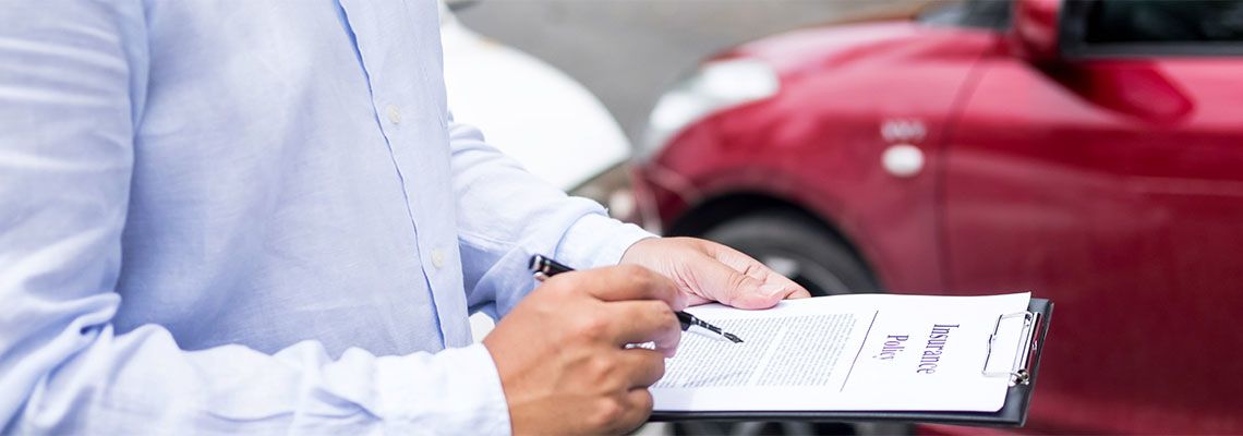 Insurance agent writing on clipboard while examining car after accident