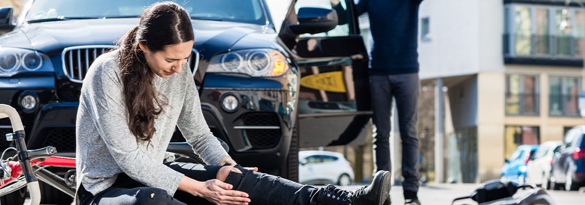 Person on the ground holding leg next to car