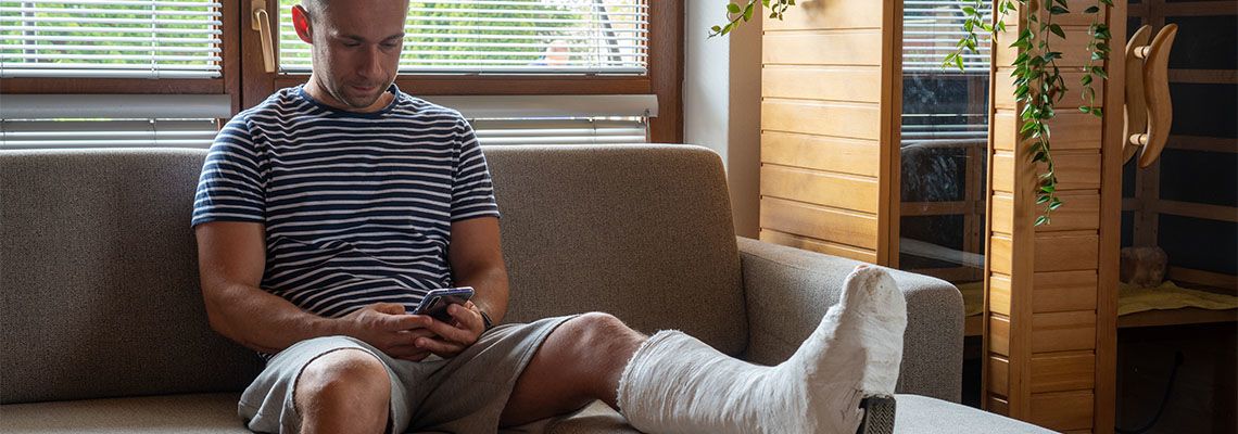 Man with broken leg in cast using mobile phone