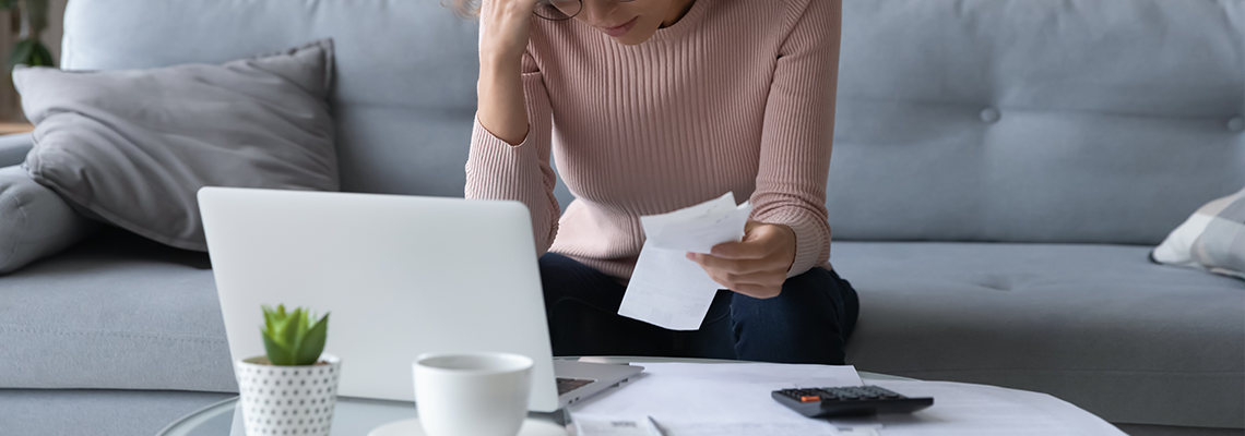 Unhappy young woman in glasses feeling stressed calculating monthly expenses at home.