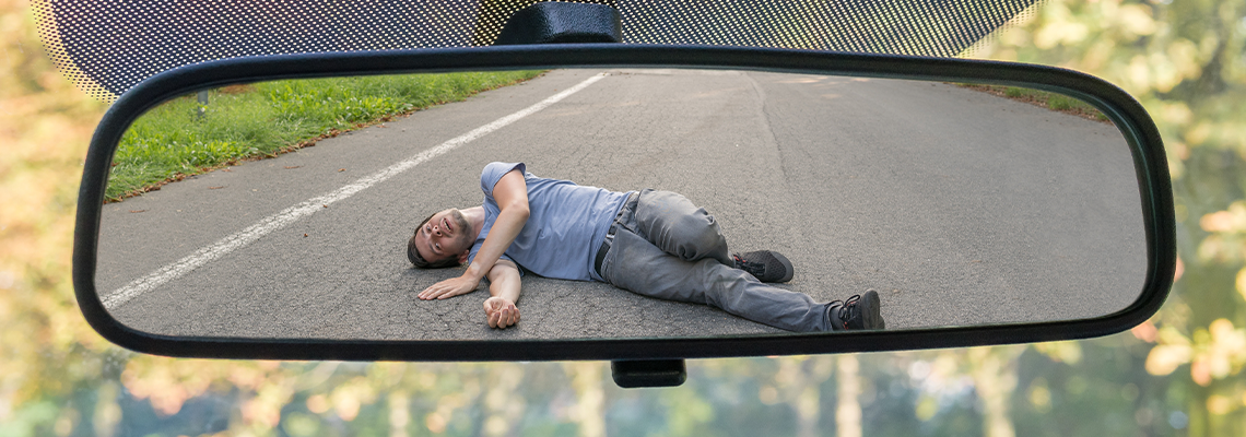 View on injured man on road in rear mirror of a car