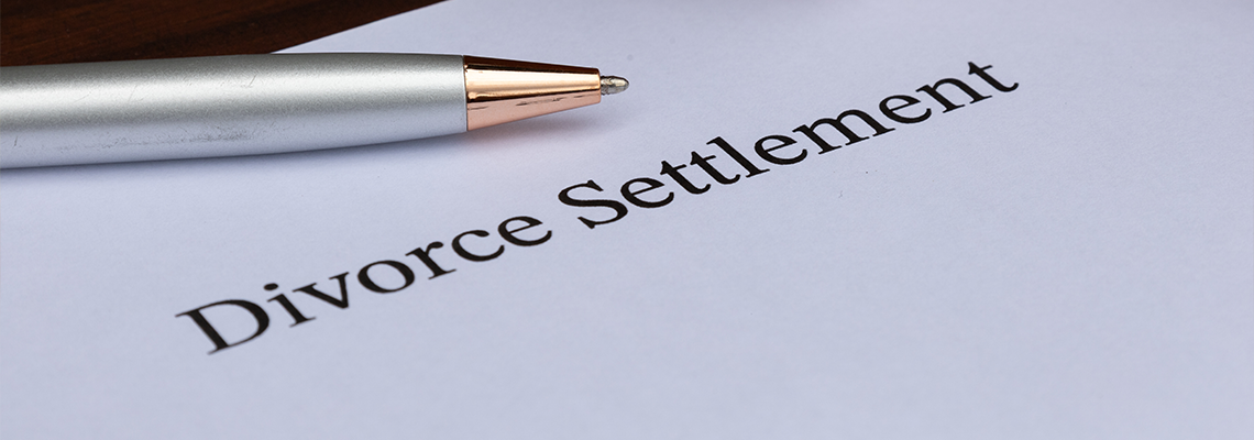 A divorce settlement paper placed beside a gavel and pen on a warm wooden surface