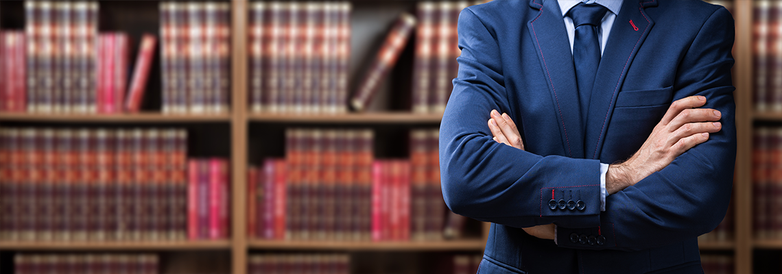 Person with arms crossed in front of a bookshelf