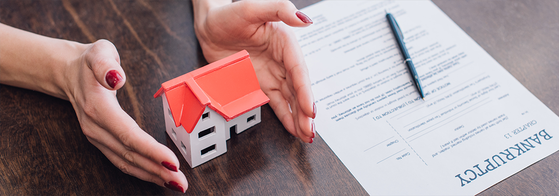 Woman protecting a small house and a bankruptcy form
