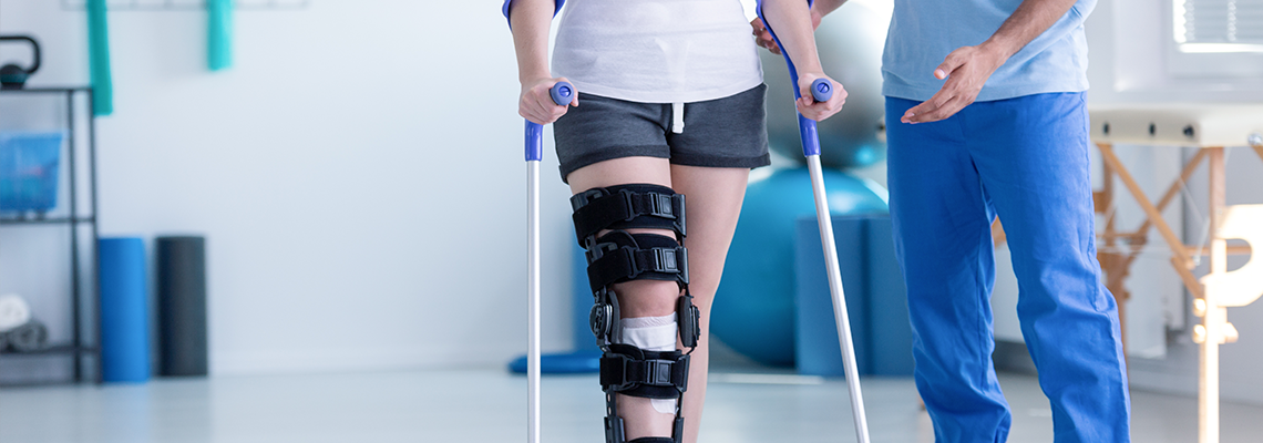 Sport physiotherapist and patient with leg injury during training with crutches.