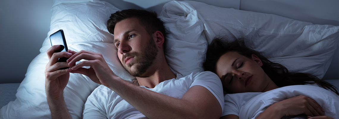 Man Using Cellphone While His Wife Sleeping On Bed