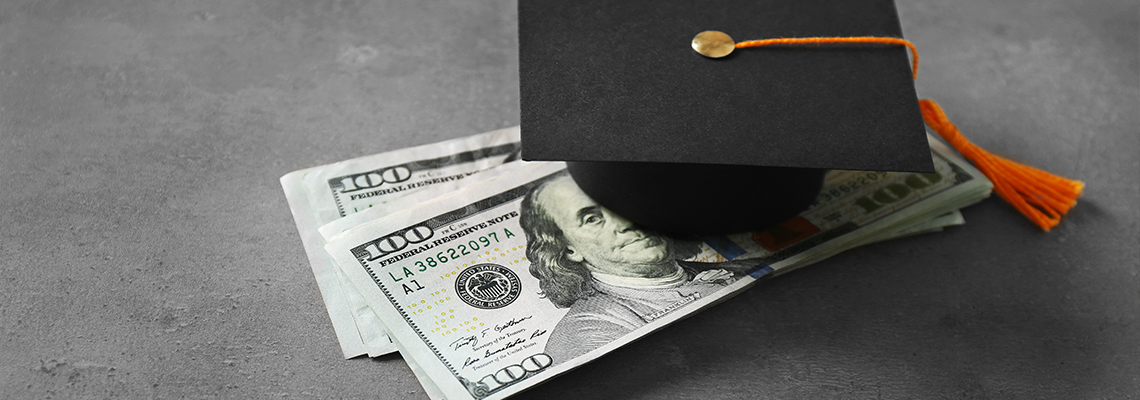 Graduation hat and dollar banknotes on table.