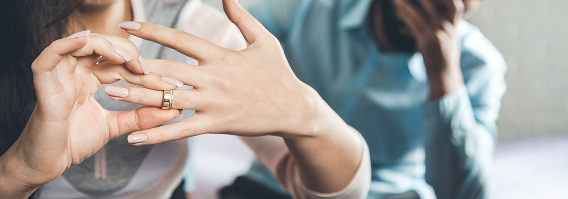 close up of a woman taking a wedding ring off her finger with sad man