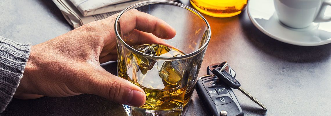 Glass of alcohol in mans hand next to car keys