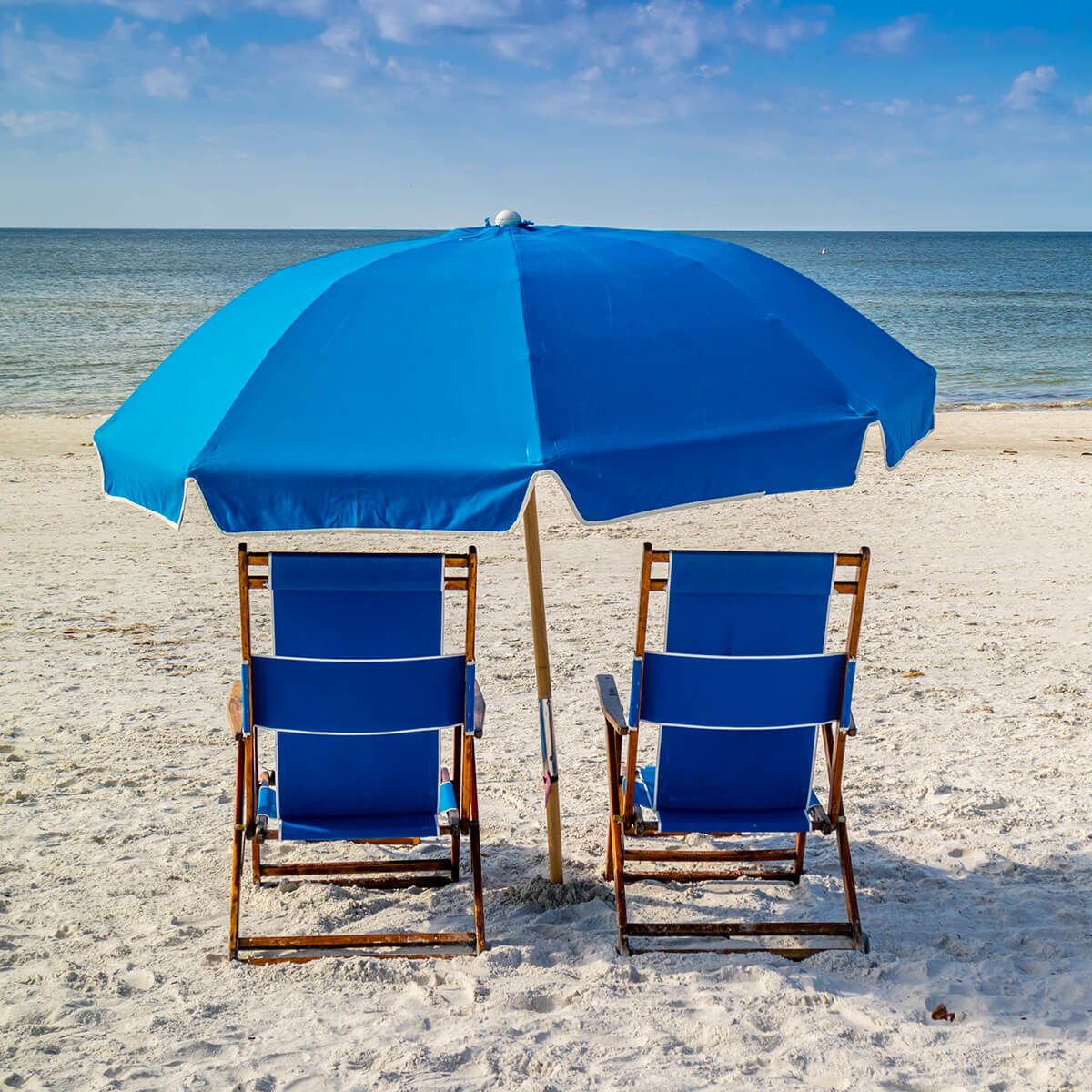 Two umbrella covered blue chairs by the beach