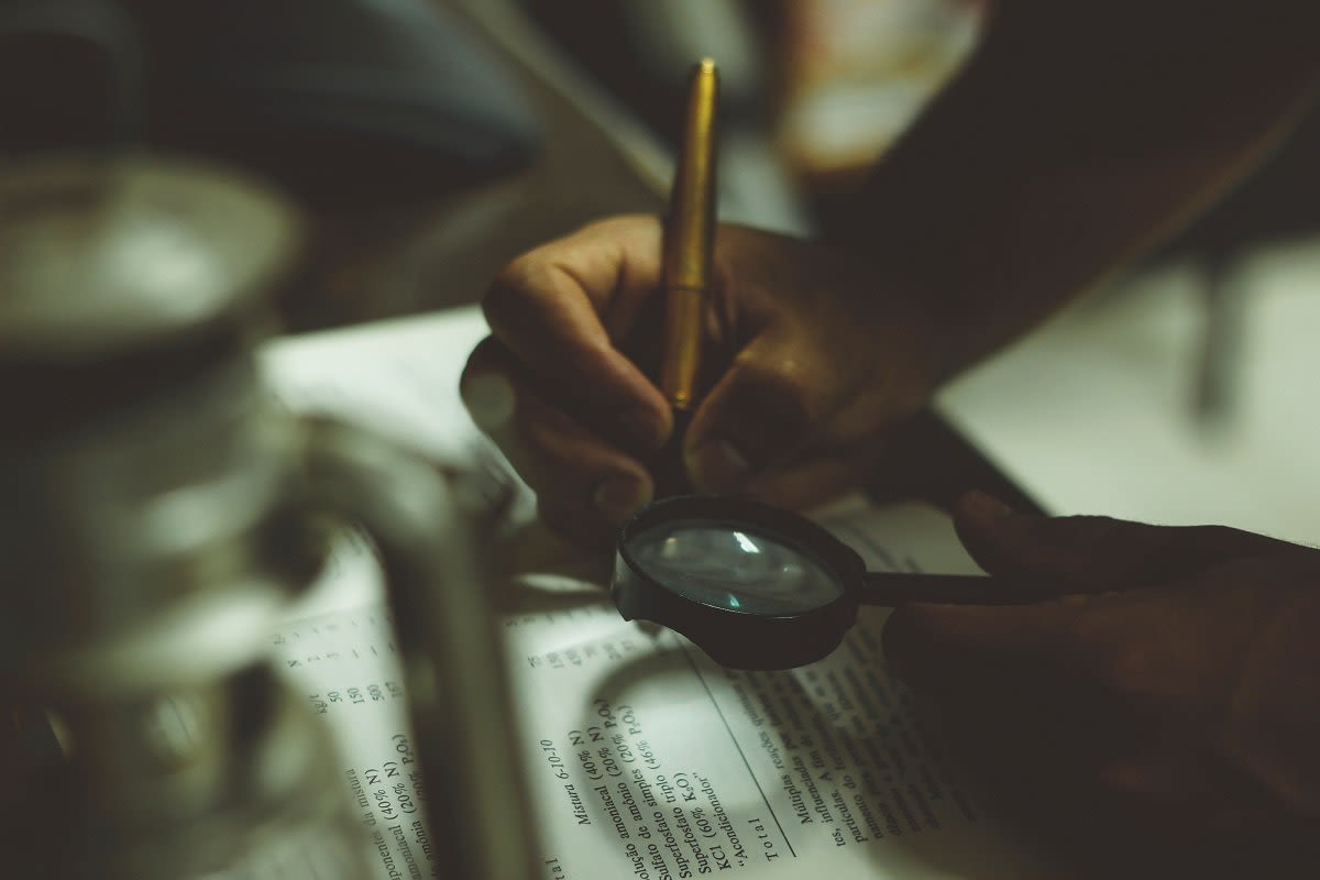 Man Writing and Looking at the Magnifying Glass