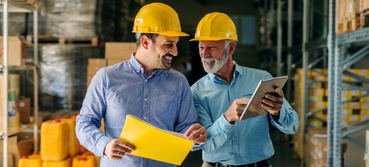 older and younger man in construction hats looking at tablet
