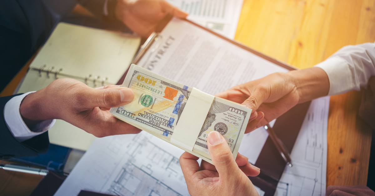 A picture of two people transferring a stack of dollar bills over a contract and documents