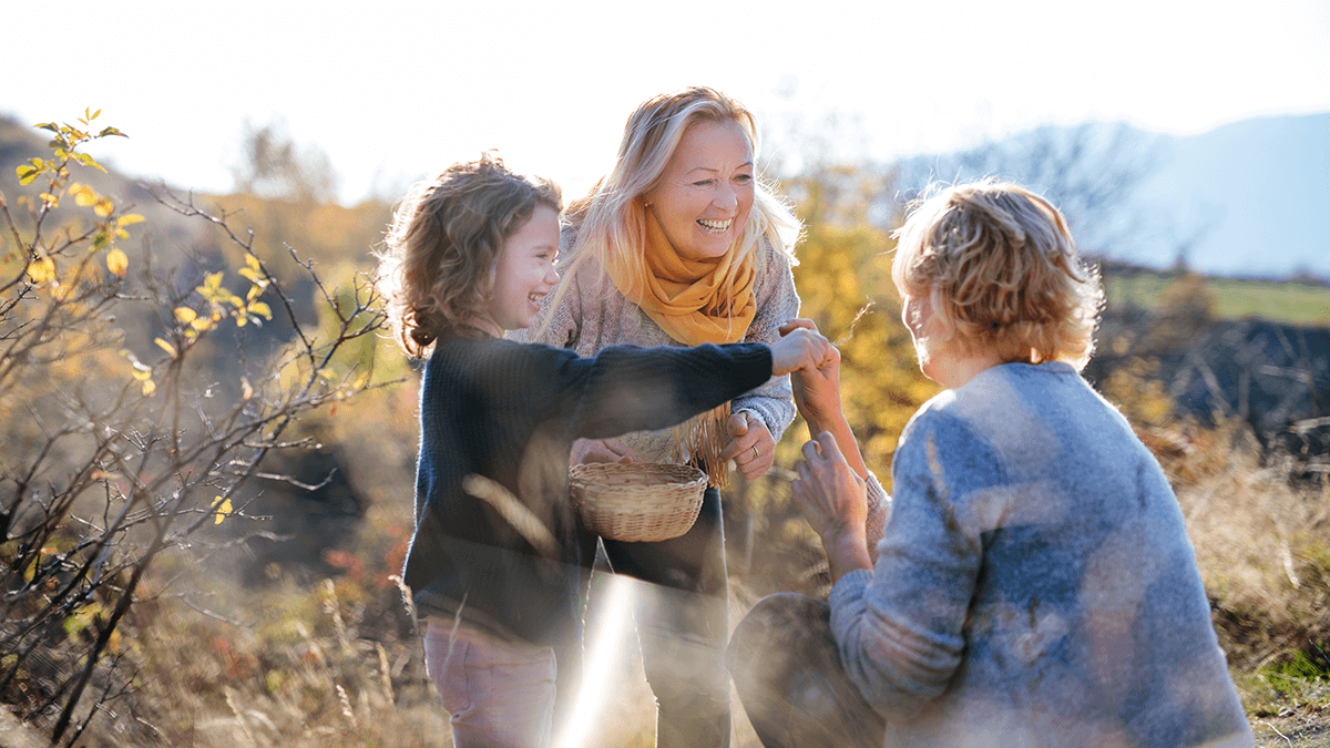 a grandma and granddaughter greeting the mother of the child in a sunny field