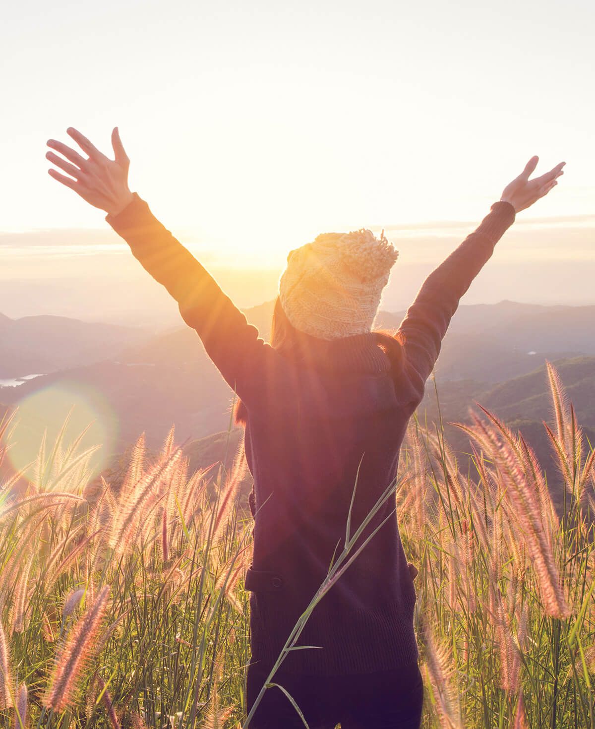 A woman celebrating with her hands up in a sunny field.