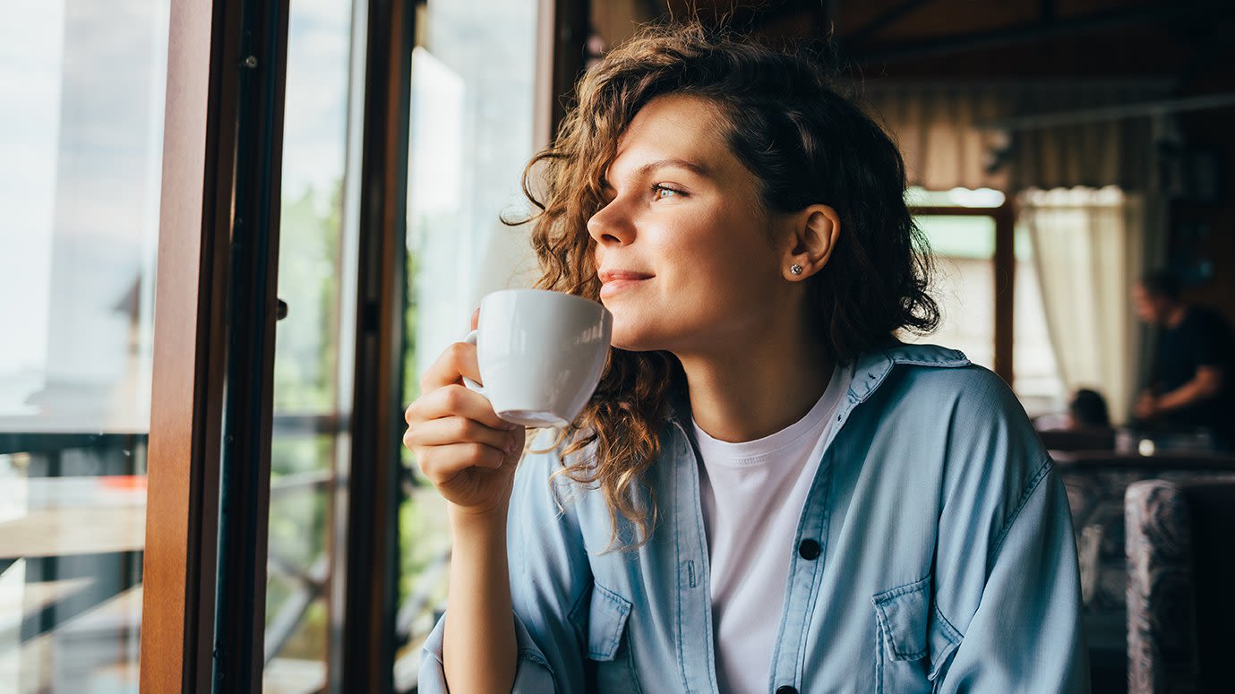 Woman drinking a cup of coffee and looking out a sunny window