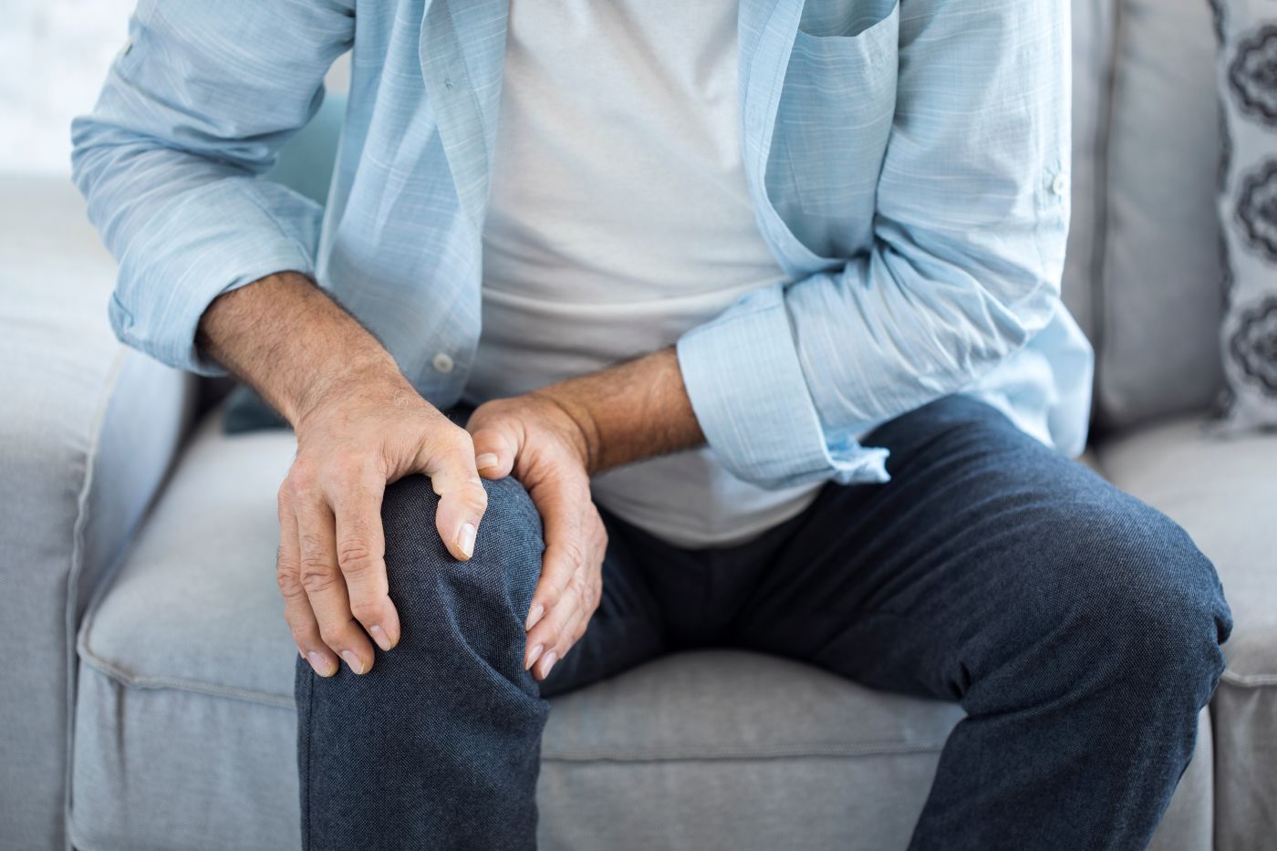 man sitting on couch holding knee after injury
