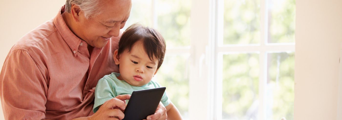 Grandparent holds grandchild while looking at tablet