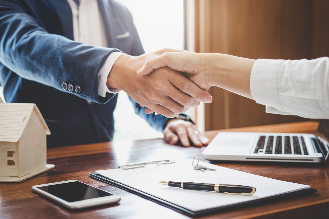 Two people shaking hands over a desk