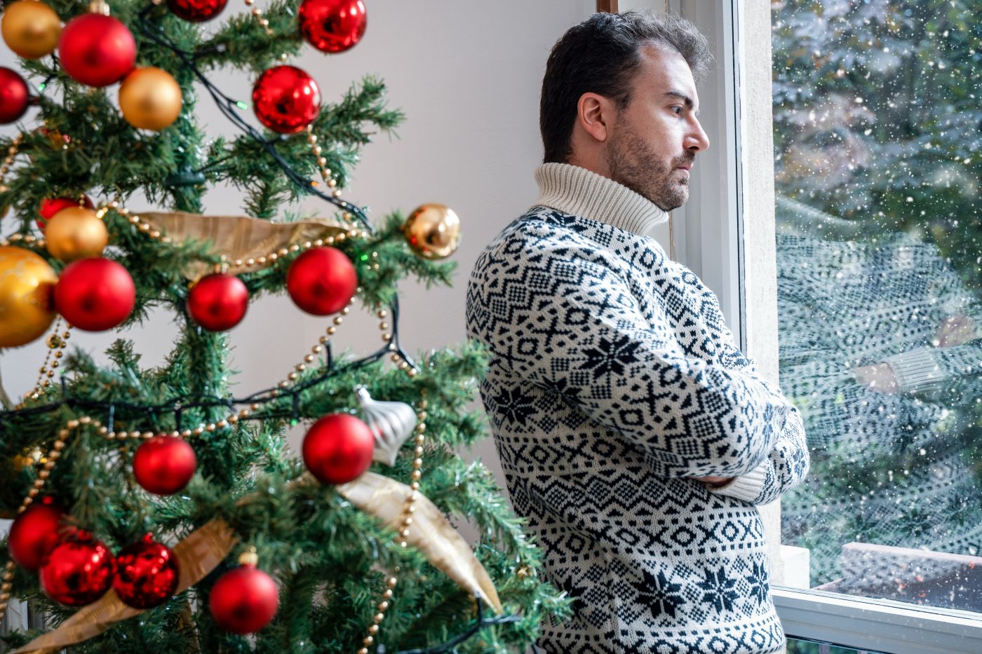 Sulking Man in Festive Sweater Next to Christmas Tree