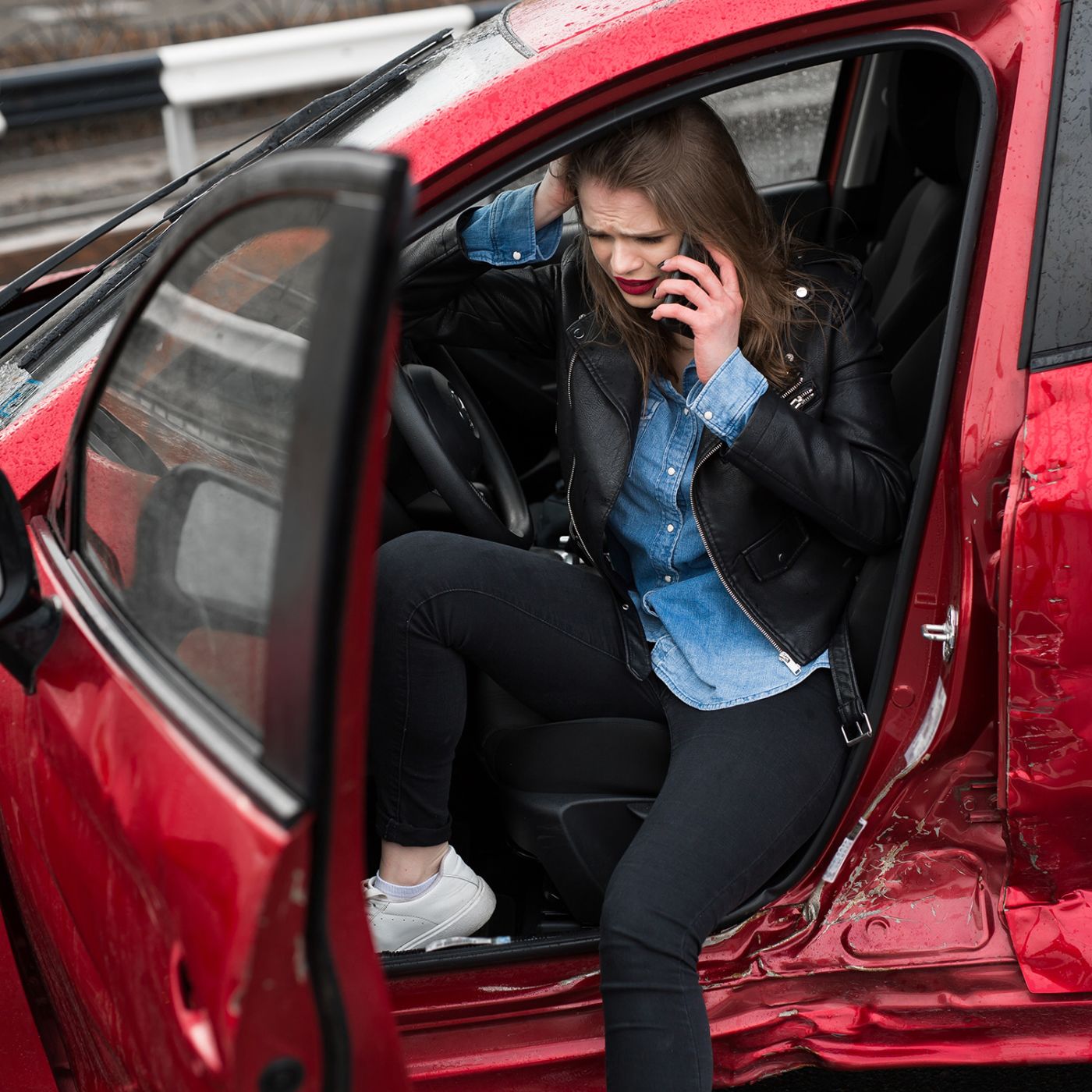 A woman in her car on her phone after a serious car accident.