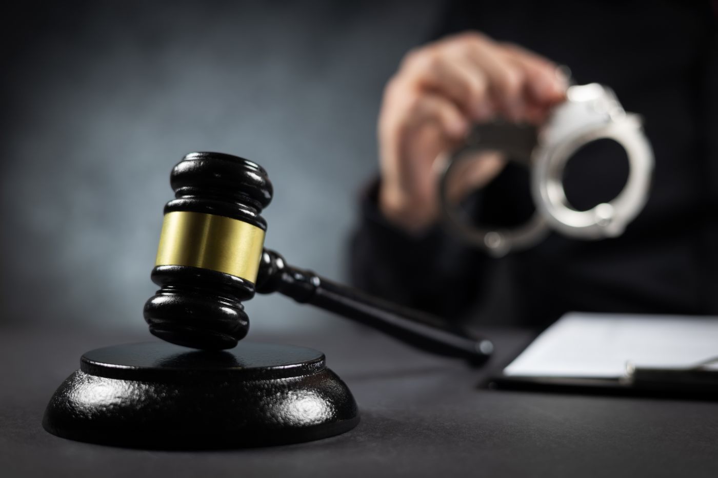 Gavel on table with man holding handcuff in background