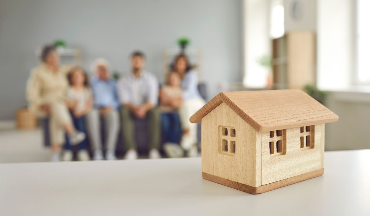 Small wooden house in table with large family in background