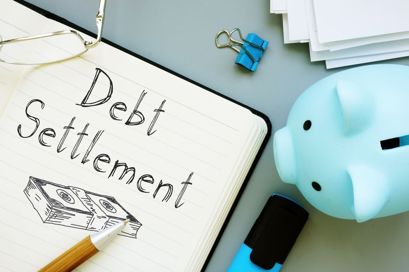 Debt Settlement word written on notebook along with piggy bank