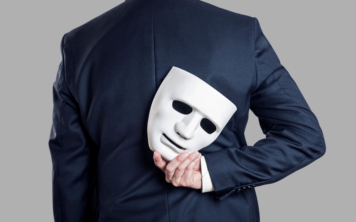 Businessman holding mask behind back, consumer deception concept image
