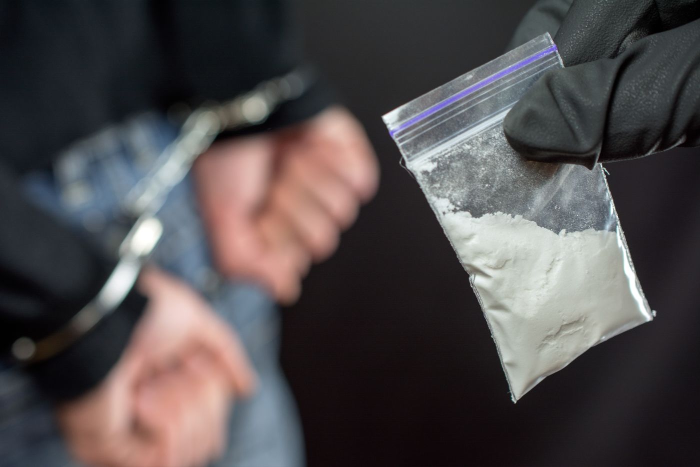 Handcuffed man and pouch of drug in police hand