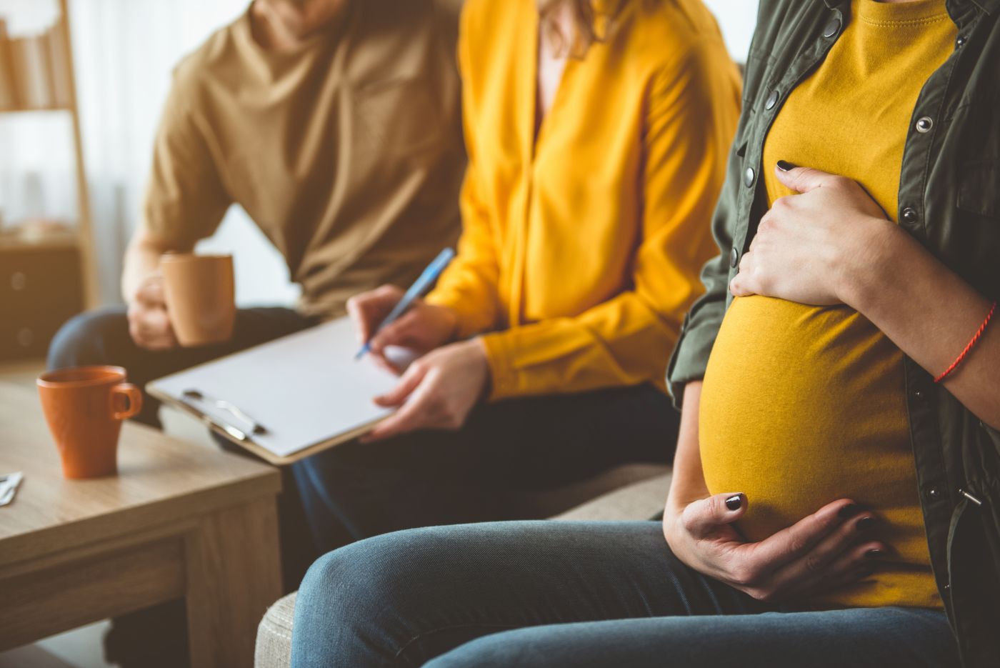 Pregnant women touching abdomen with couples signing agreement in back