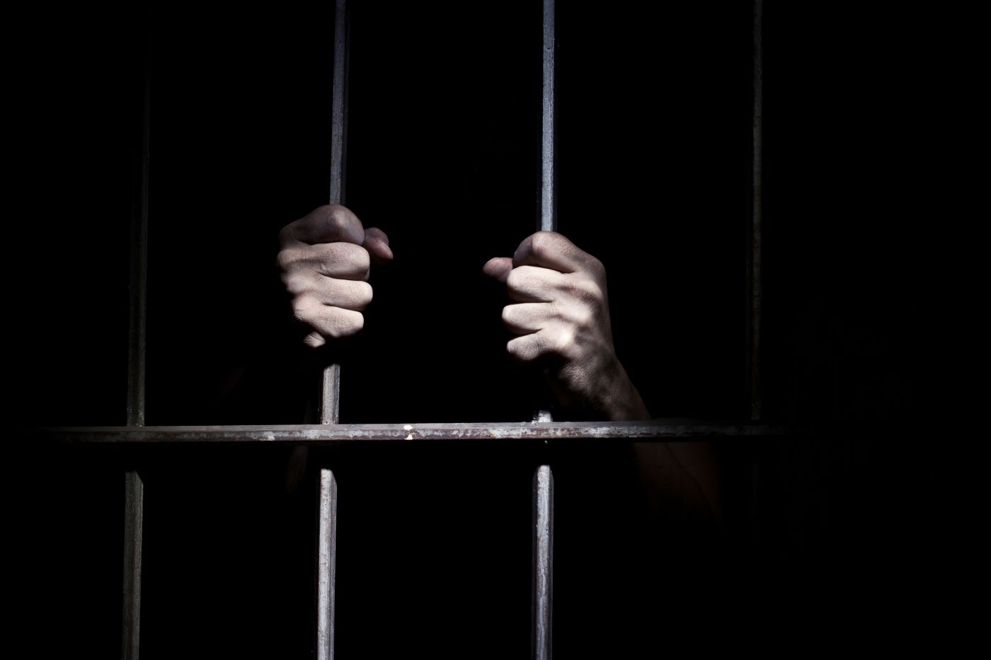 Hands of person behind jail bars