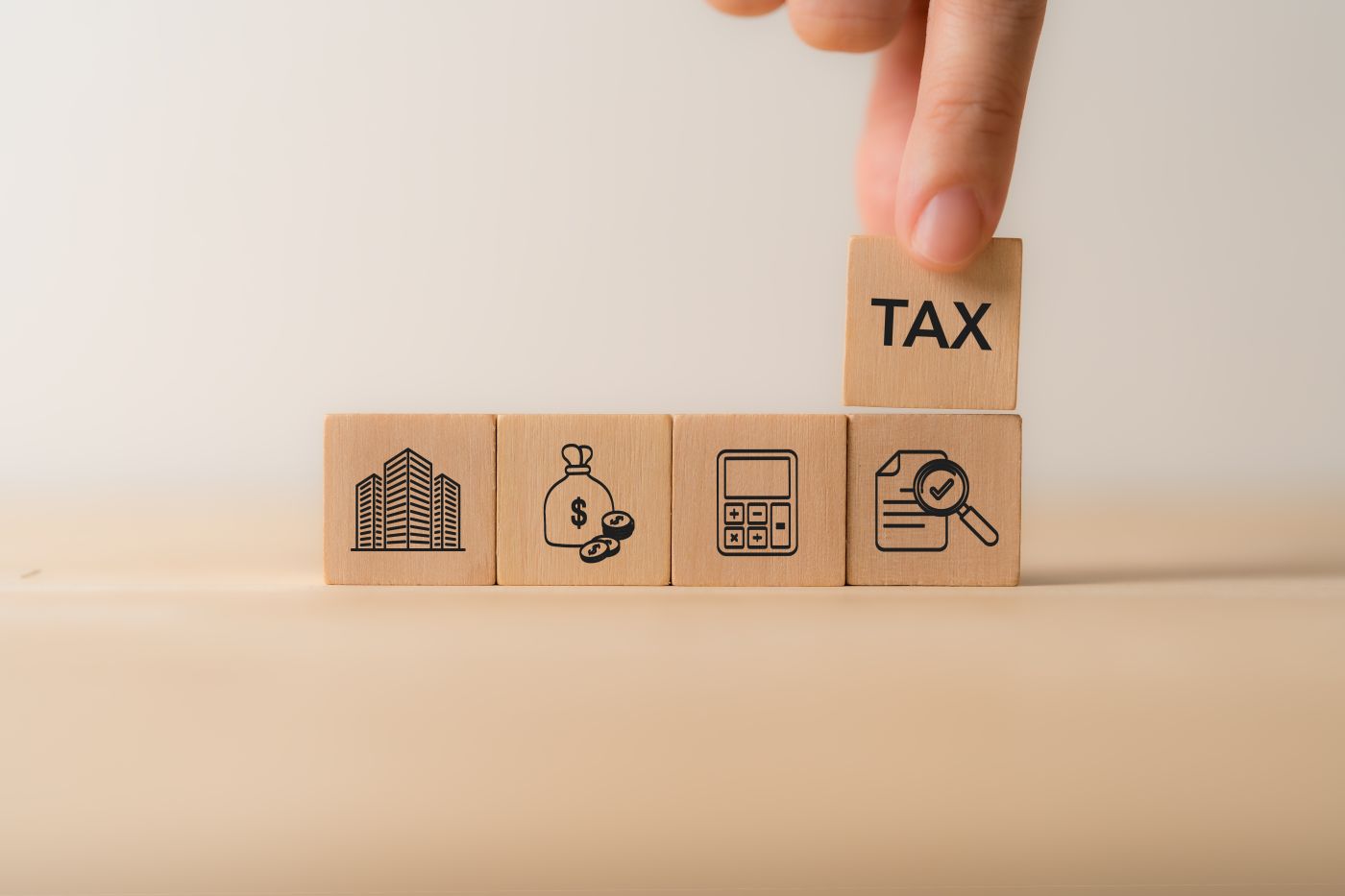 A hand stacking wooden blocks with tax-related icons