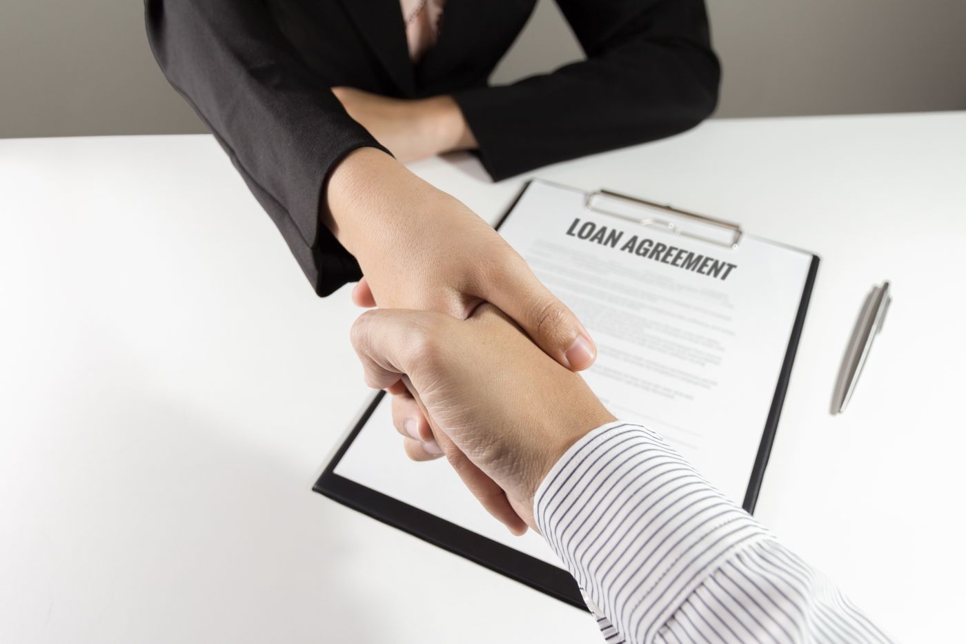 Two parties shaking hand over loan agreement document