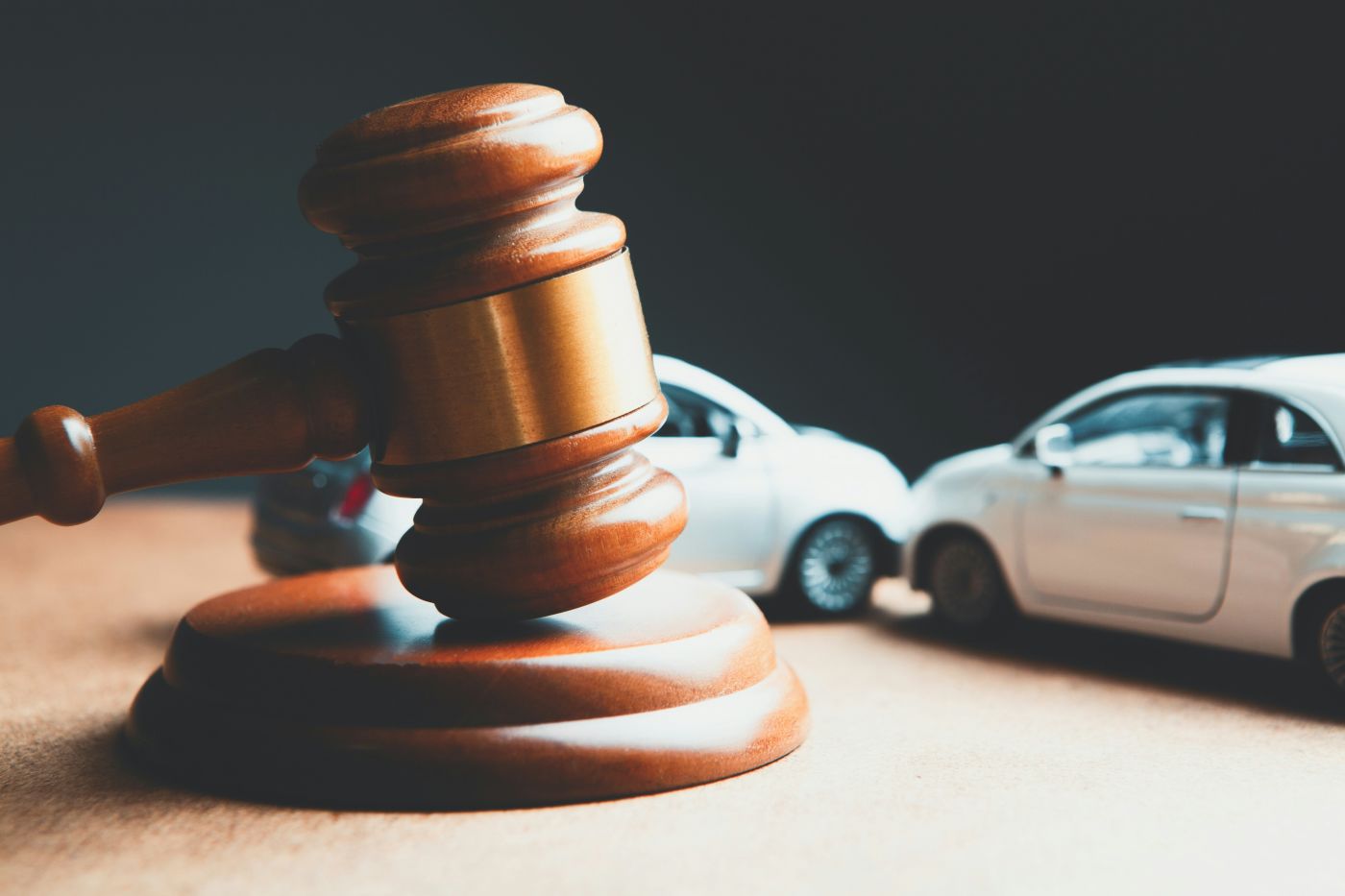 Two white toy cars on wooden desk next to judge gavel