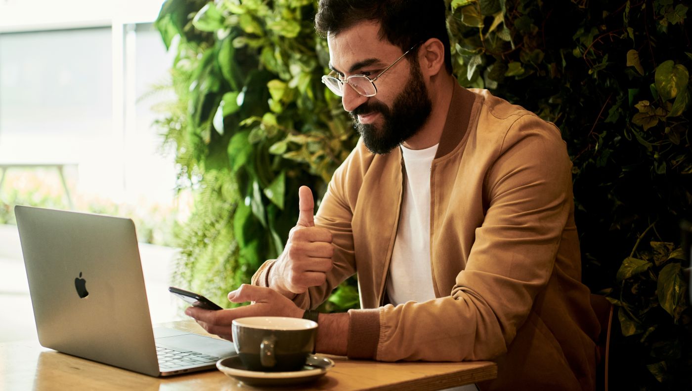 Middle Eastern male employee giving a thumbs up while on a video call in cafe