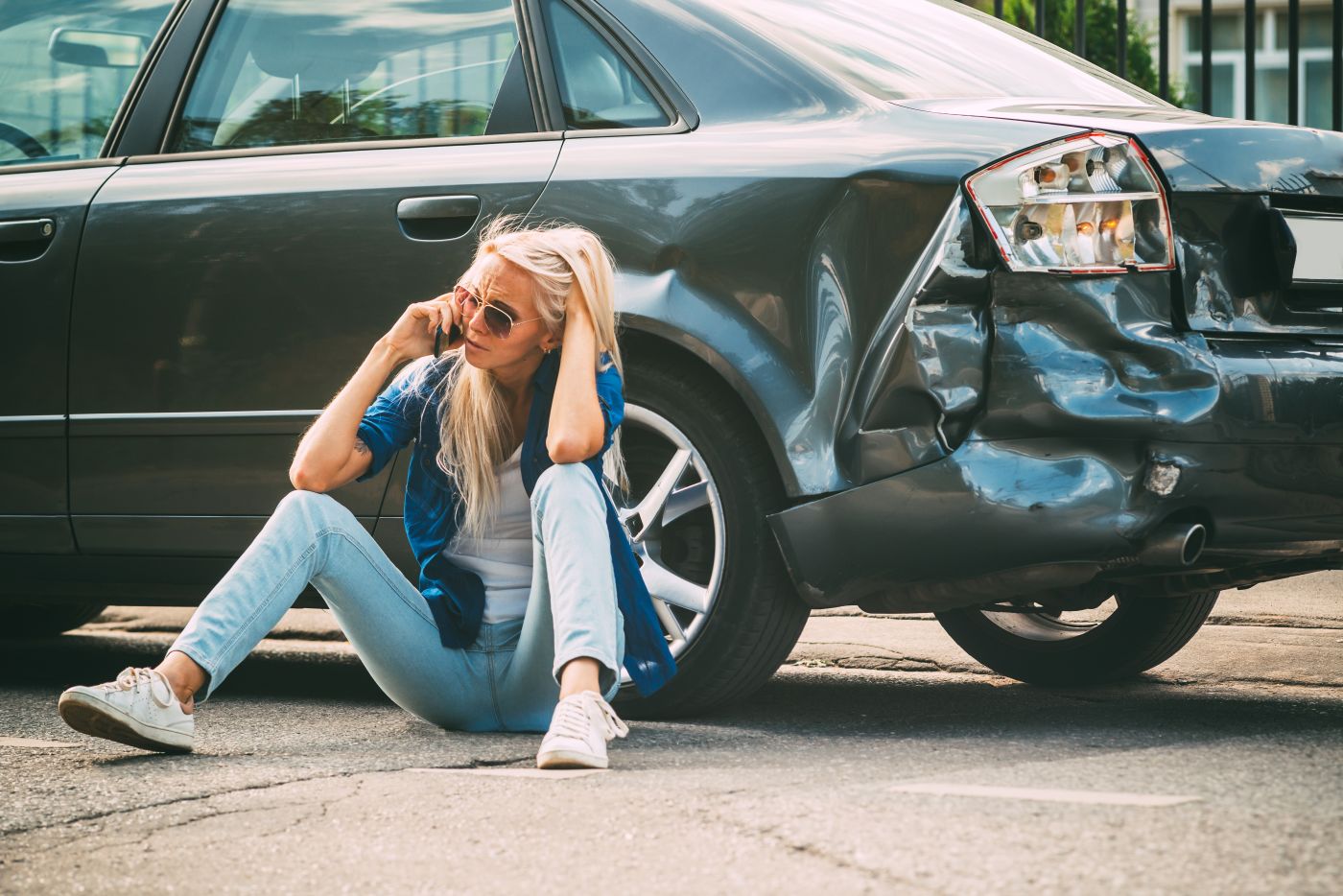 Sad women sit on road near her damaged car