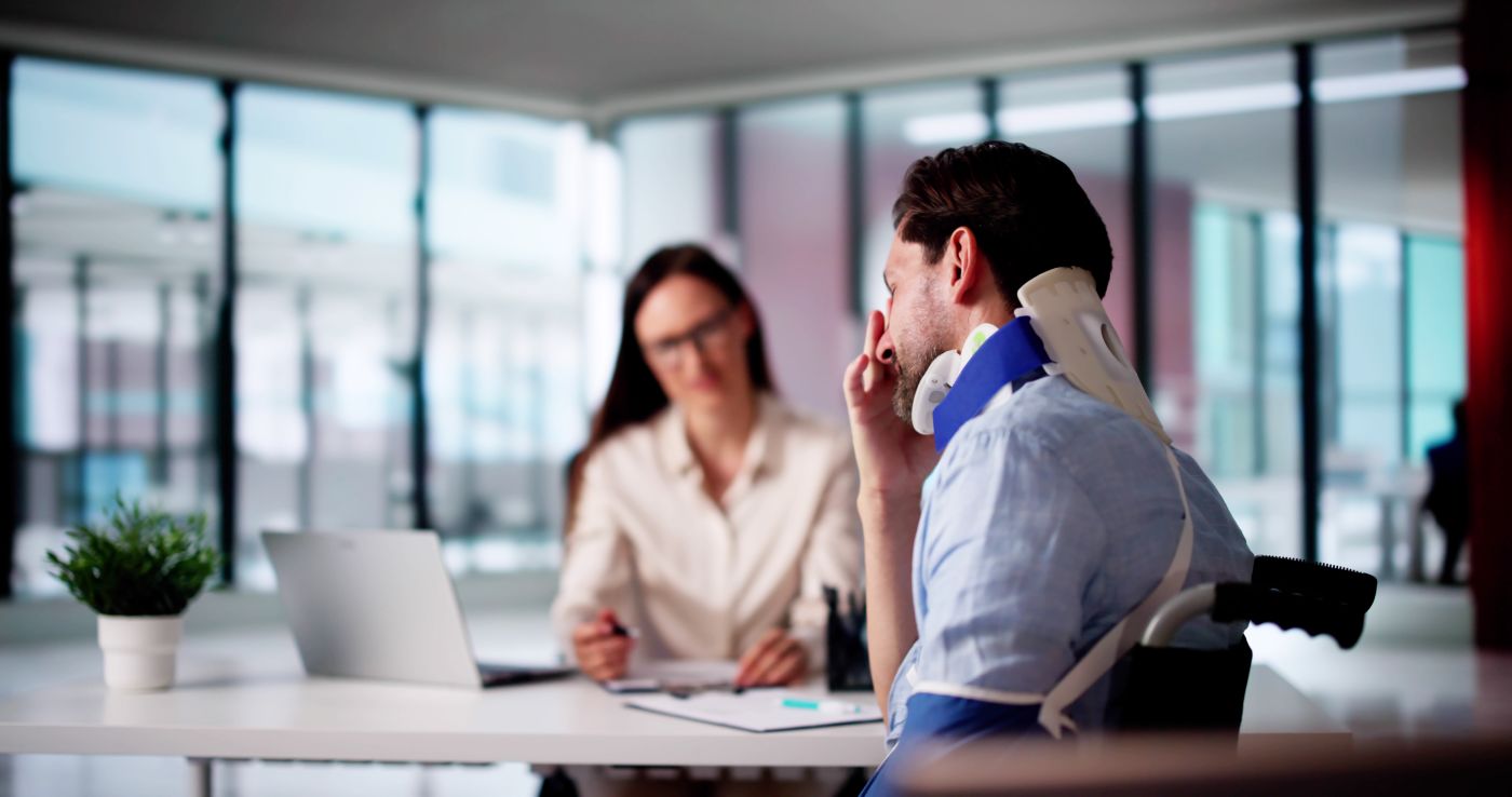 man with neckbrace in wheelchair meets with lawyer at desk