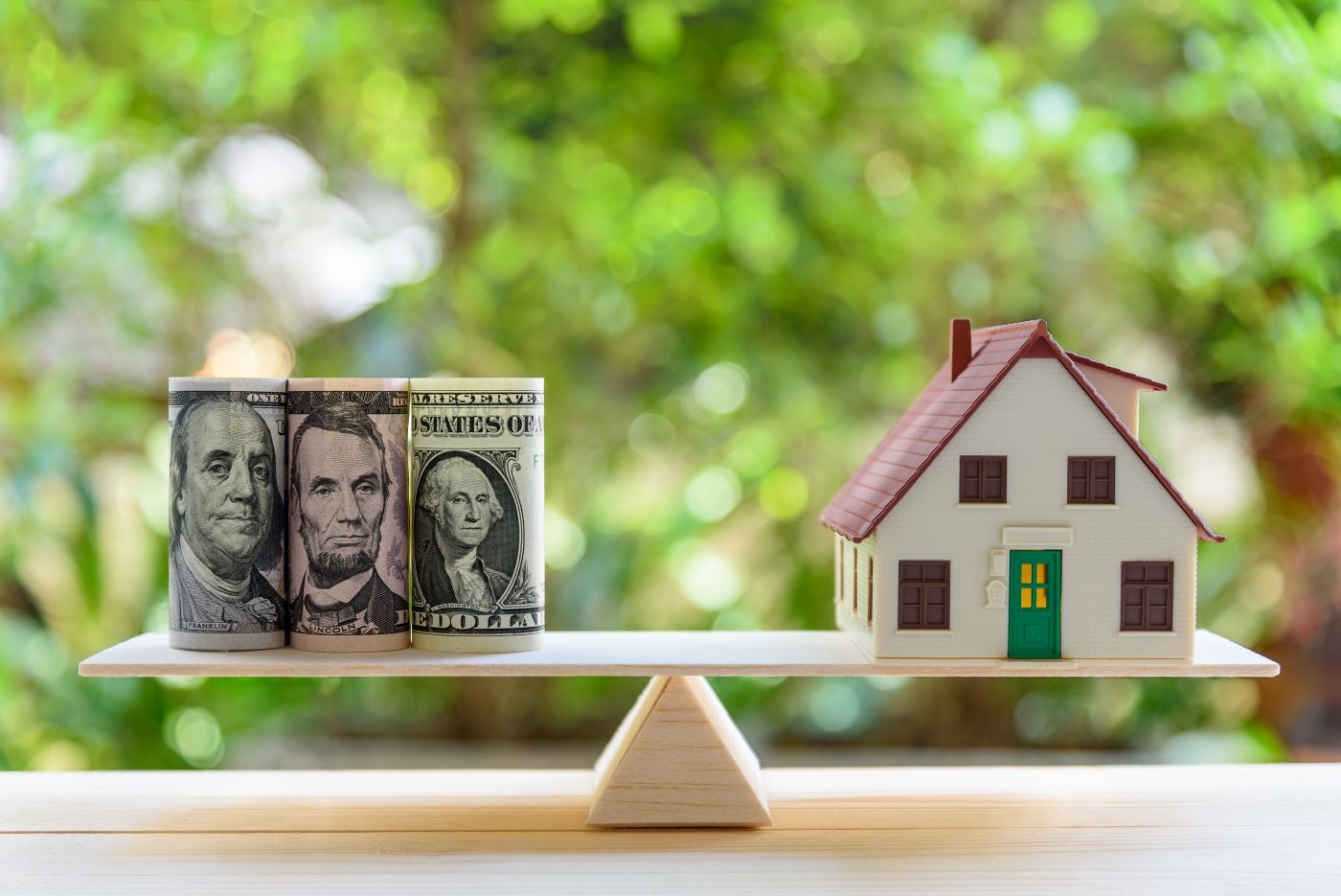 money and small plastic house on each side of a scale