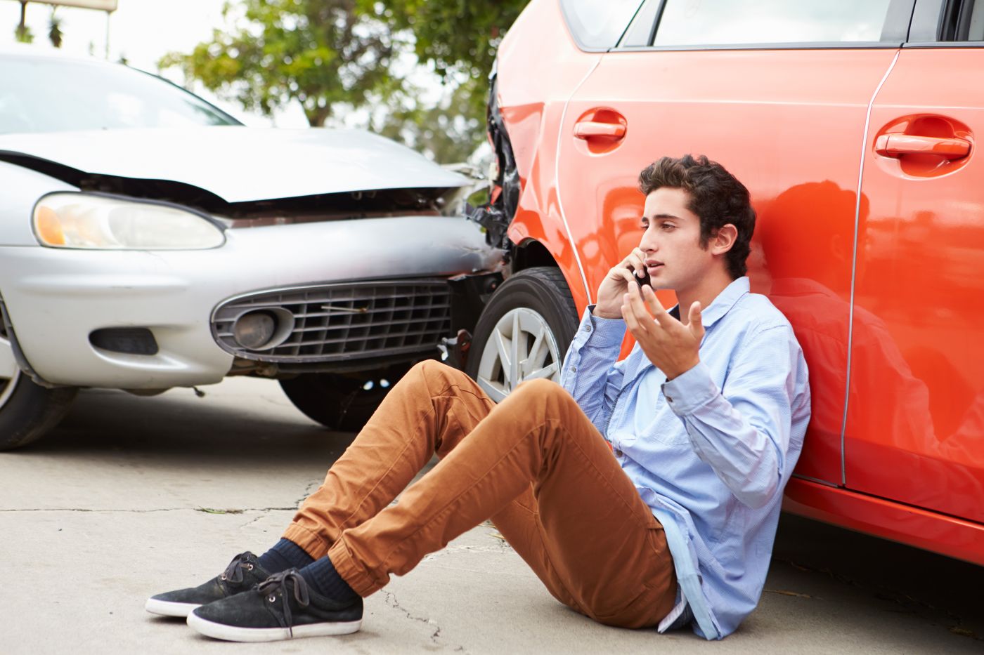 man sitting on the pavement with a car crash behind him